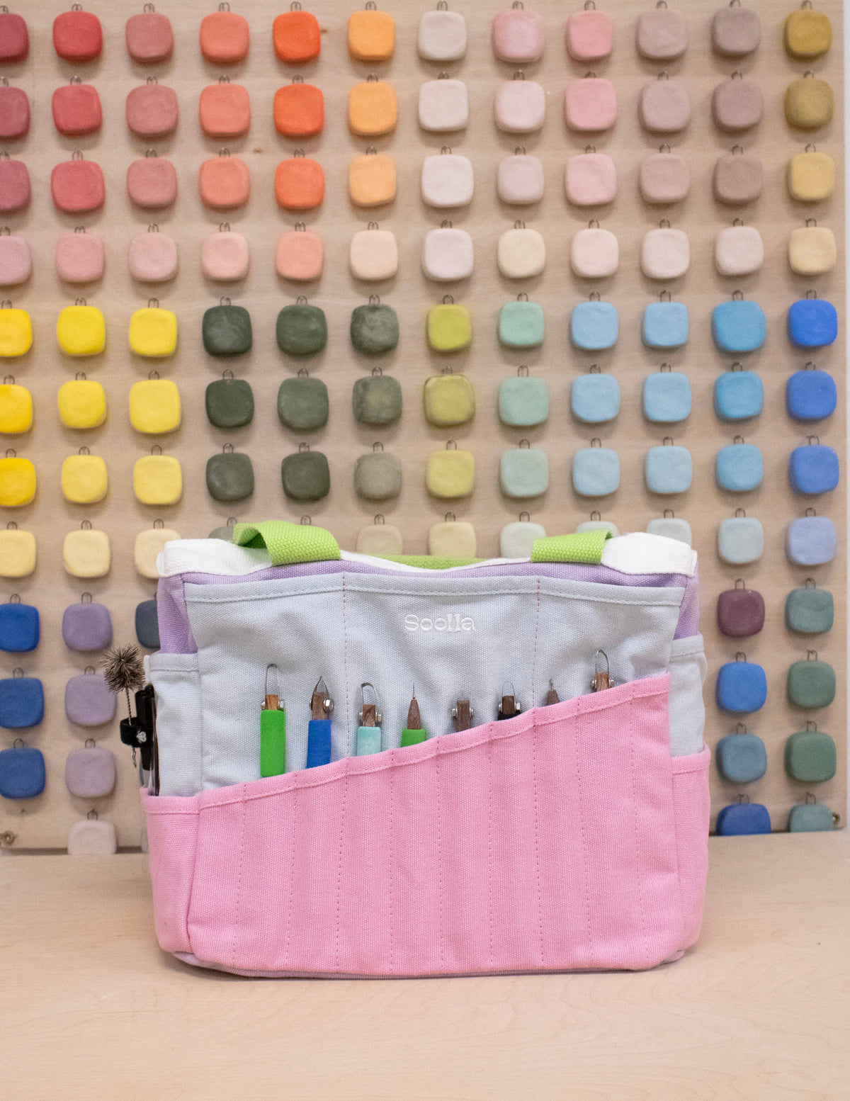 Pink craft tool organizer with colorful handles against a multicolored square patterned wall.