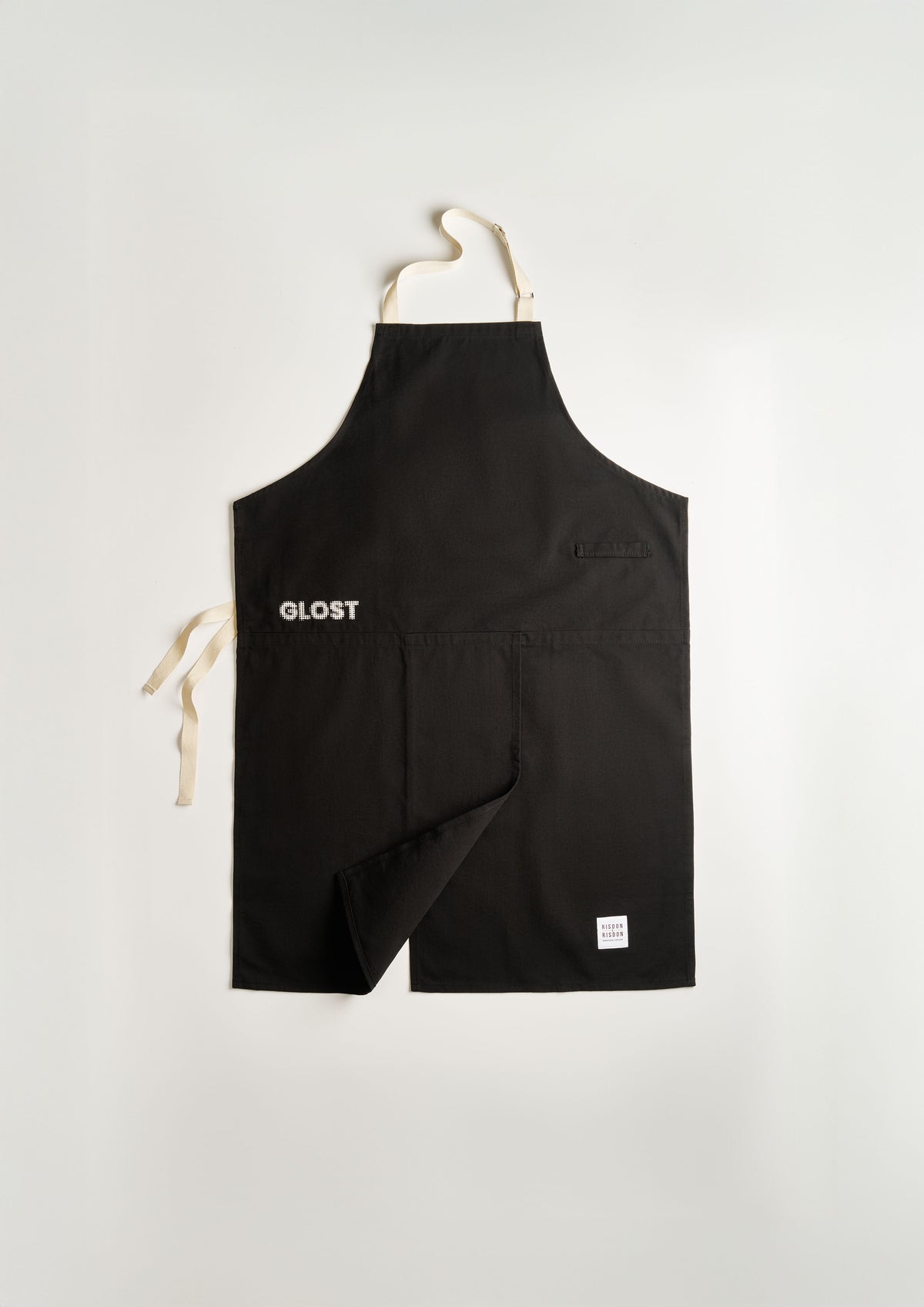 GLOST Potters Apron, handcrafted in England by Risdon x Risdon. Designed with potters in mind, this premium-quality apron features a convenient split at the bottom, providing full leg coverage while seated at the wheel. Made from durable black fabric, it combines practicality with style, highlighted by its sleek white machine embroidery. Whether in the studio or showcasing your craft, this apron delivers both comfort and a professional look.