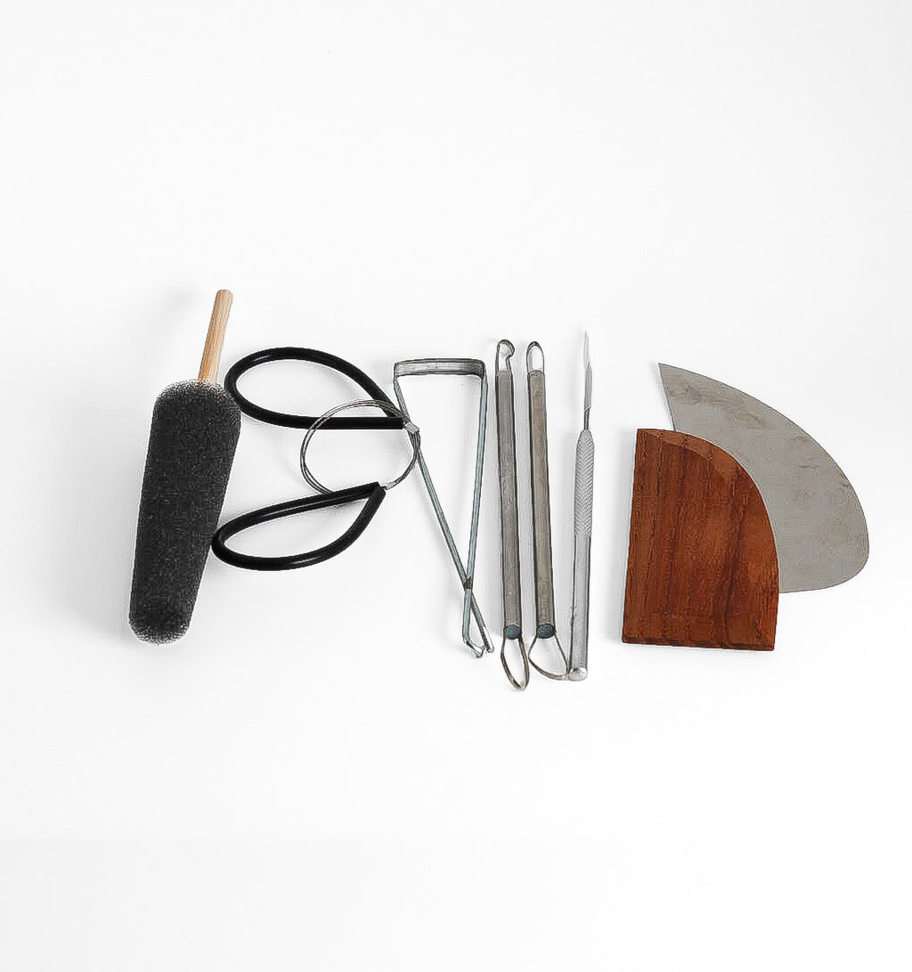 The GLOST Beginner Essentials pottery tool set laid out: sponge on a stick, steel and wooden kidneys, wire, pin tool, loop trimmers and a small bicycle trimmer.