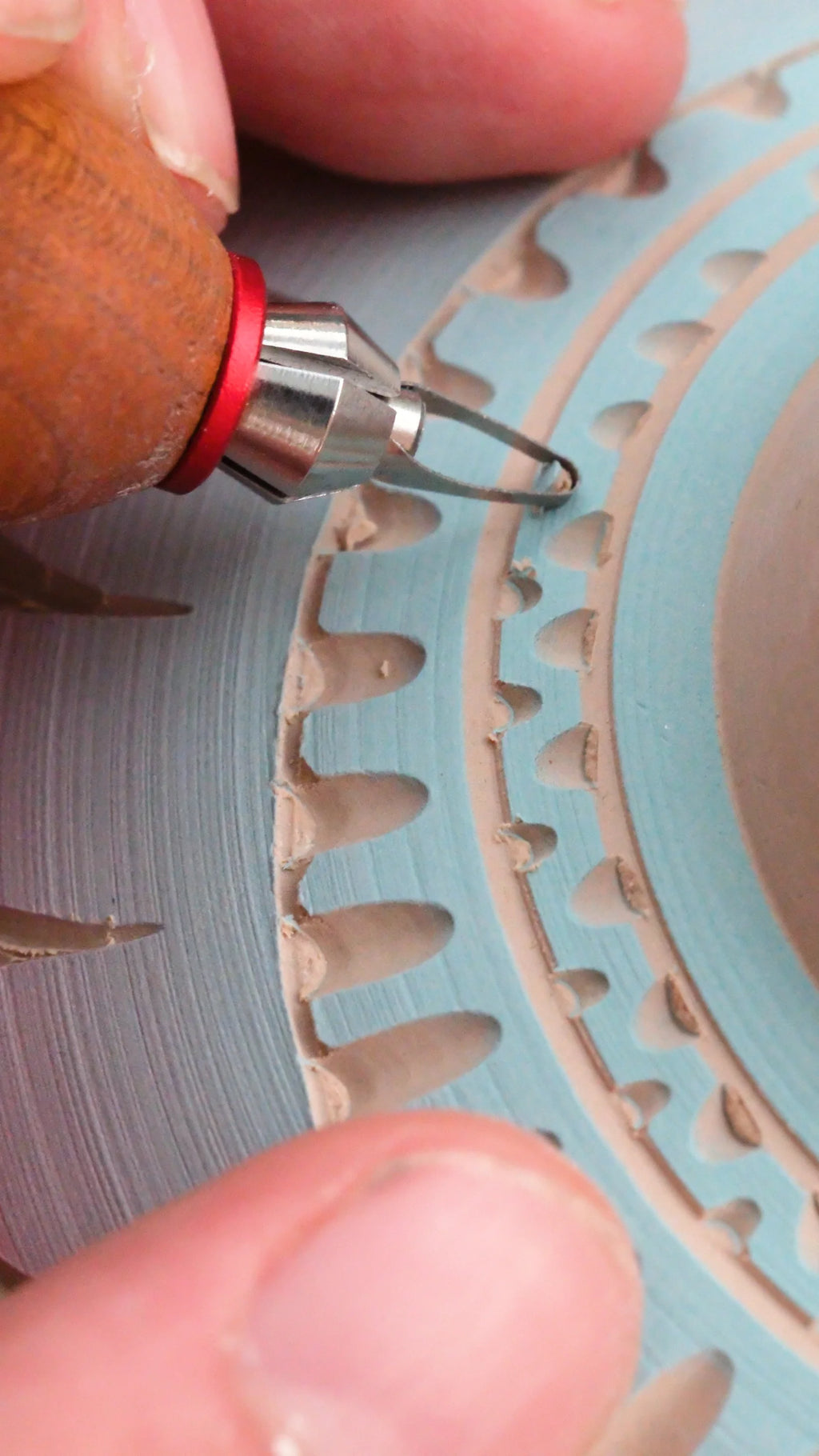 A BuschKraft Dragonfly blade carving a decorative border into a plate covered in blue slip