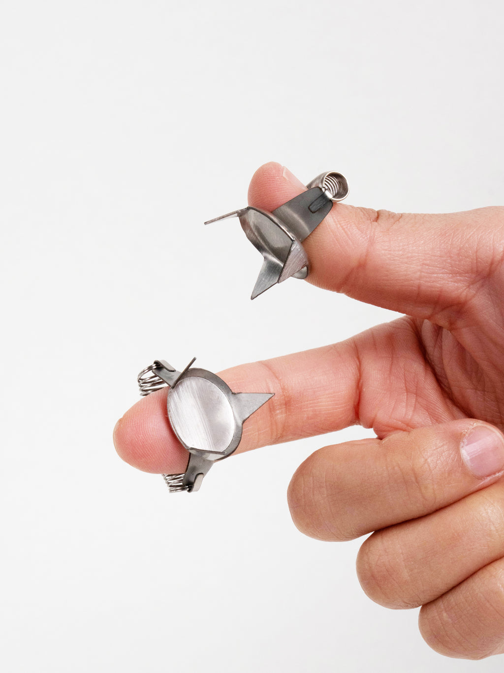 Two metal finger dipping tools clipped onto fingertips, designed for holding small ceramic items during glazing.