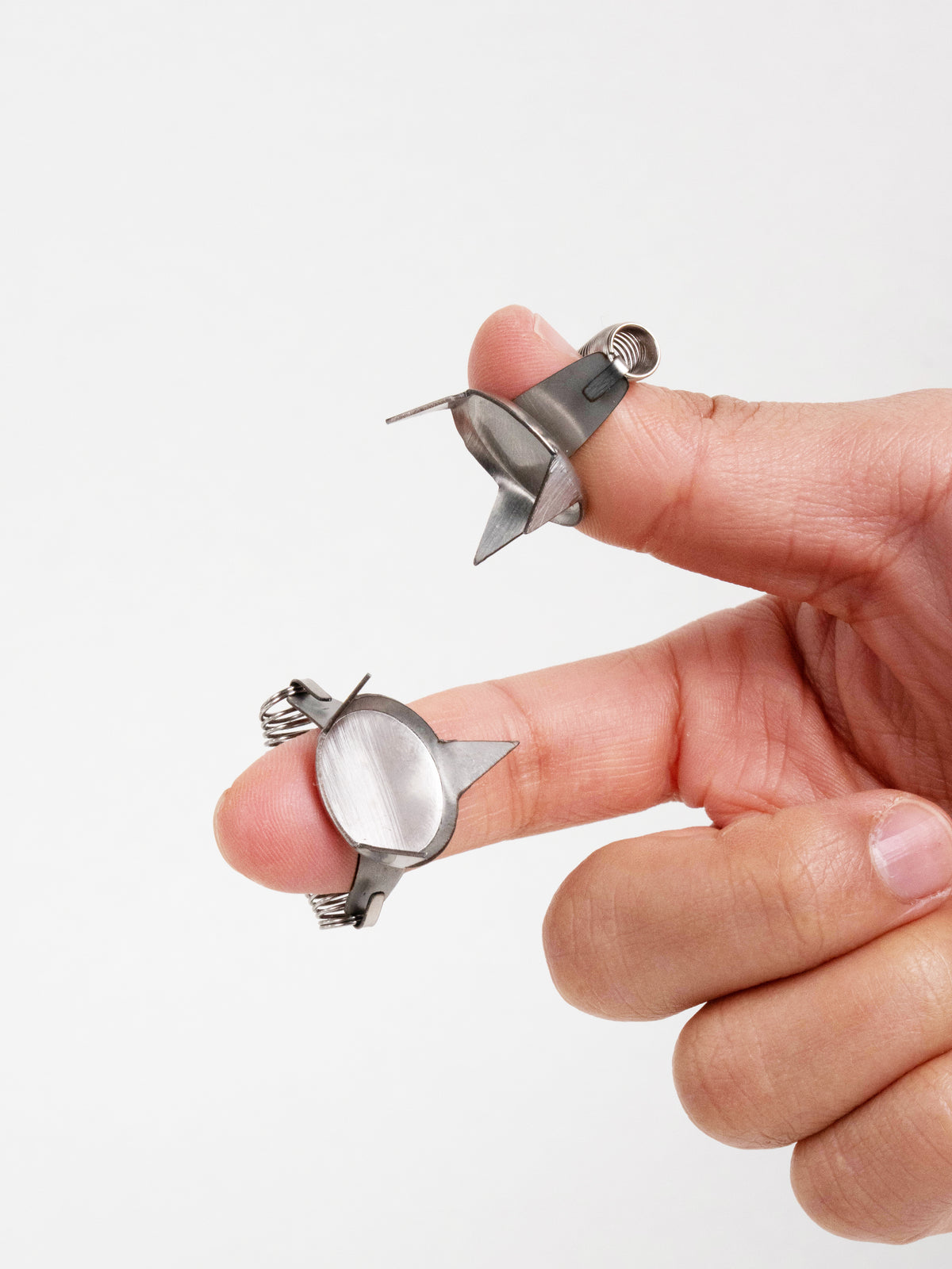 Two metal finger dipping tools clipped onto fingertips, designed for holding small ceramic items during glazing.