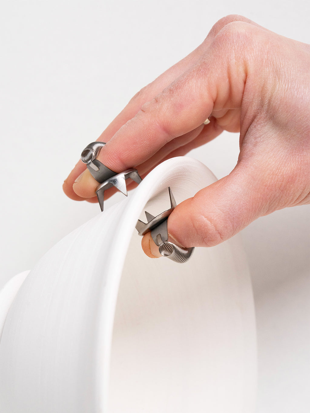 Close-up of stainless steel dipping tools with spring mechanisms, worn on fingers for precision glazing.