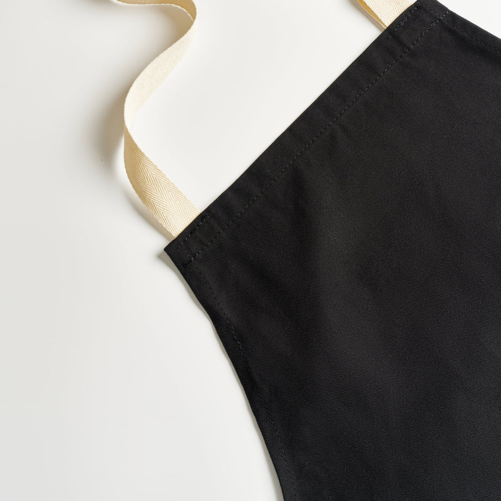 The top corner of the apron, showing the stitched edge and the cream neck strap.