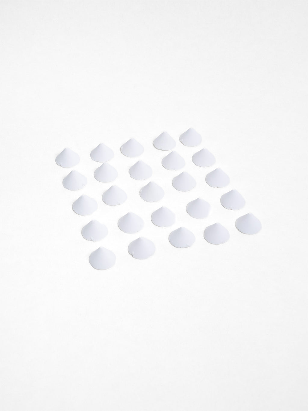 A neat grid of small white ceramic kiln stilts arranged on a flat white surface, each shaped like a low cone.