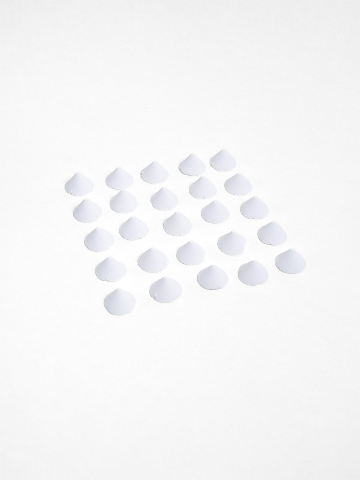A neat grid of small white ceramic kiln stilts arranged on a flat white surface, each shaped like a low cone.