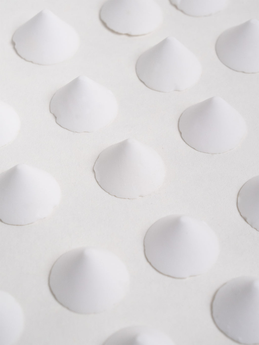 Twenty-five evenly spaced ceramic firing stilts displayed in rows, used to support glazed pieces in the kiln.