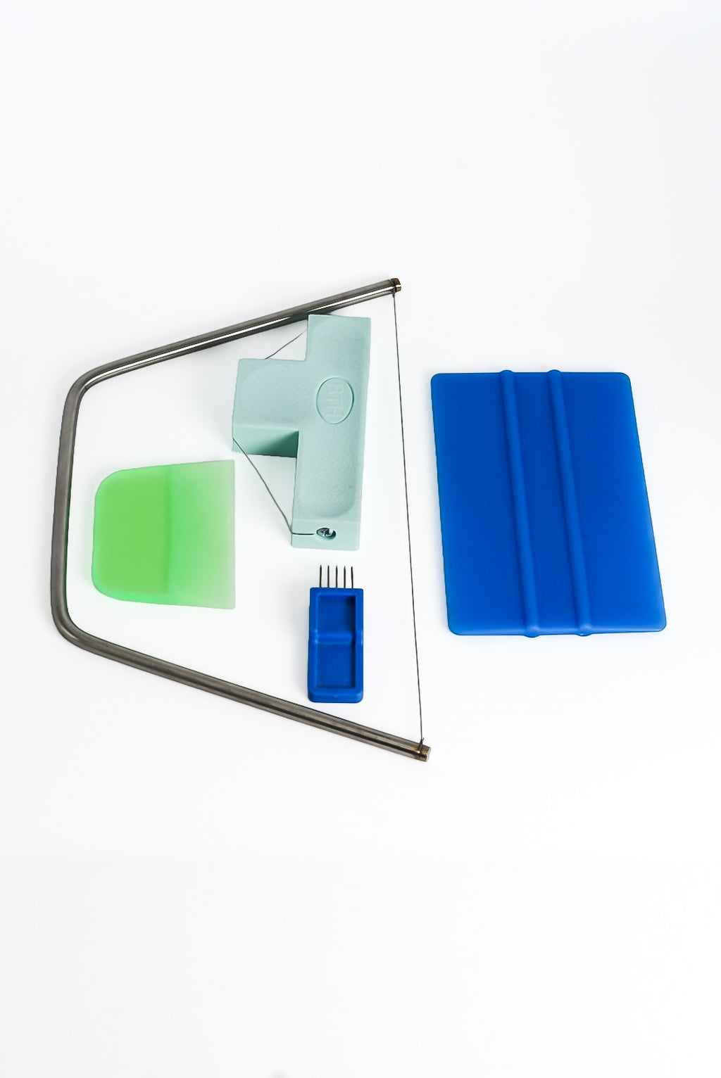 The GLOST Handbuilding tool set laid out: scoring tool, bevel wire, bow harp, blue scraper and a green rubber kidney.