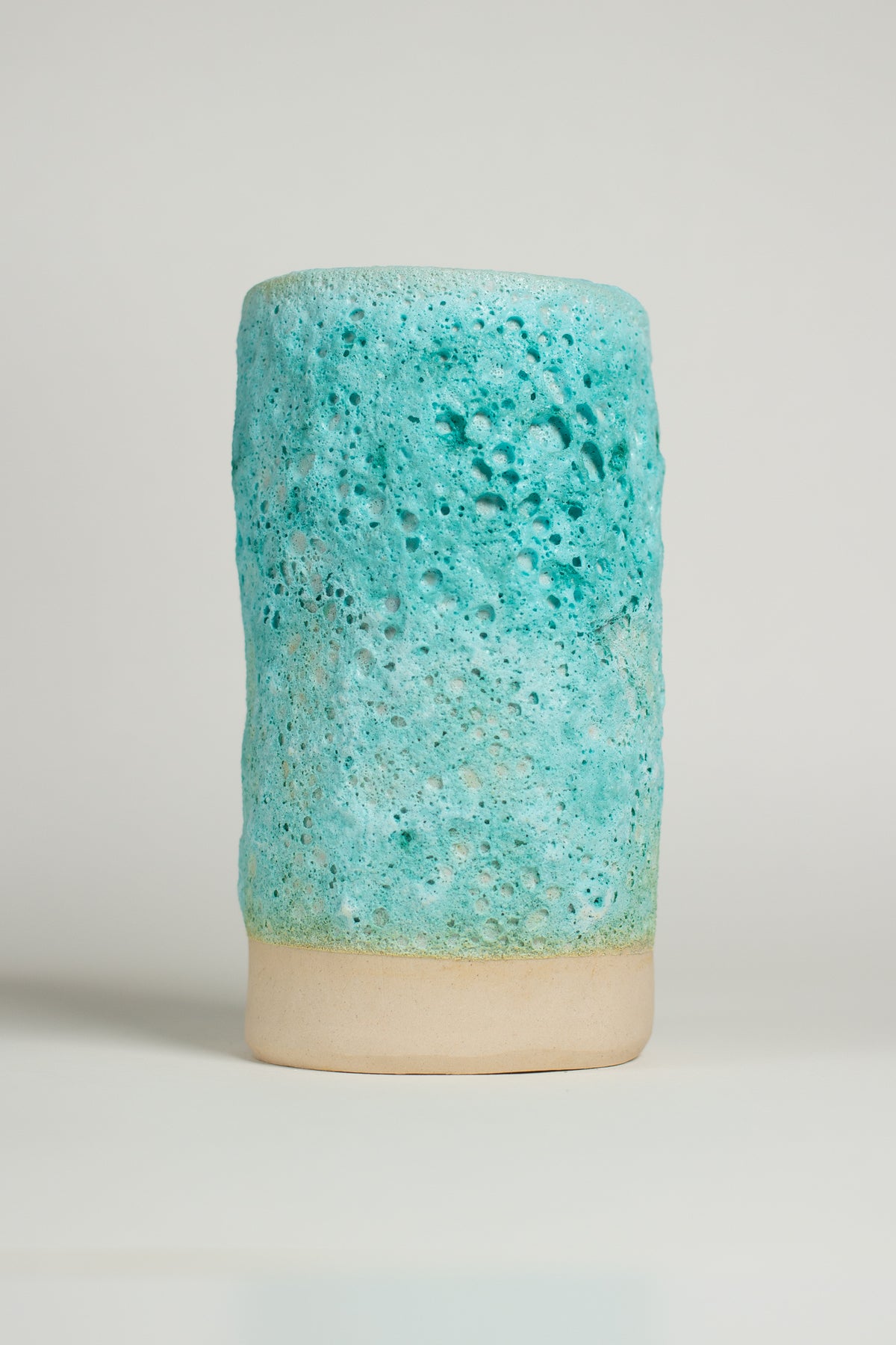 A ceramic piece with a textured surface featuring shades of turquoise lava glaze and light green.