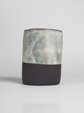 Milky Matt White on a thrown cylinder of dark clay, pale grey-white matt with iron speckle over a raw black foot