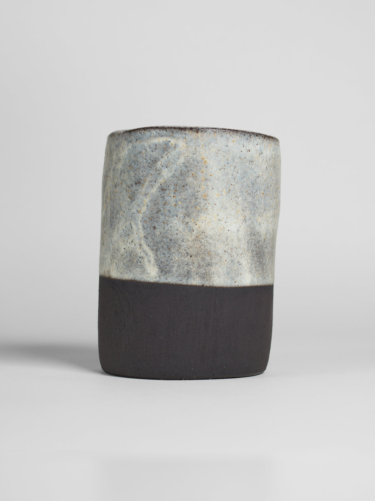 A handmade ceramic object with a tall, cylindrical shape. The upper portion is glazed with milky matt white. The cylinder features an artistic, organic design with a matte finish.