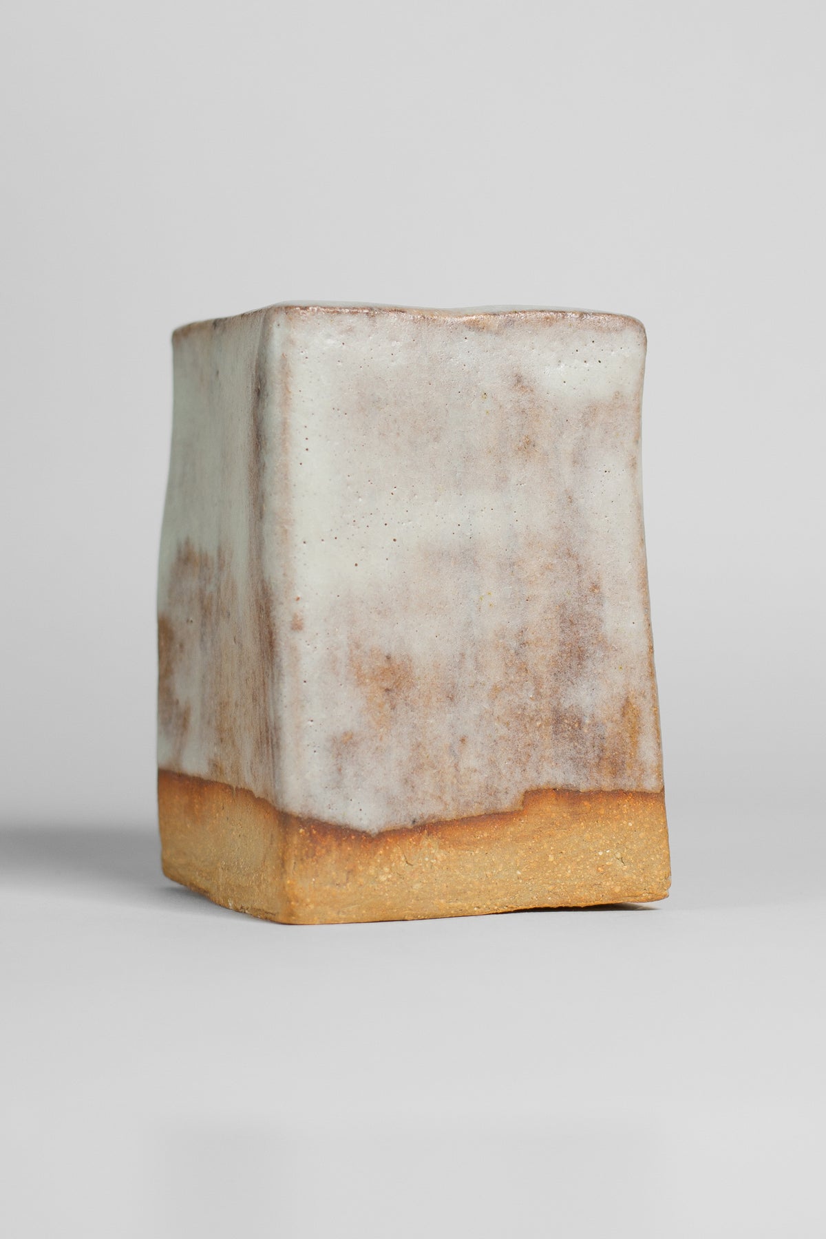 A handmade ceramic object with a tall, cylindrical shape. The upper portion is glazed with milky matt white. 
