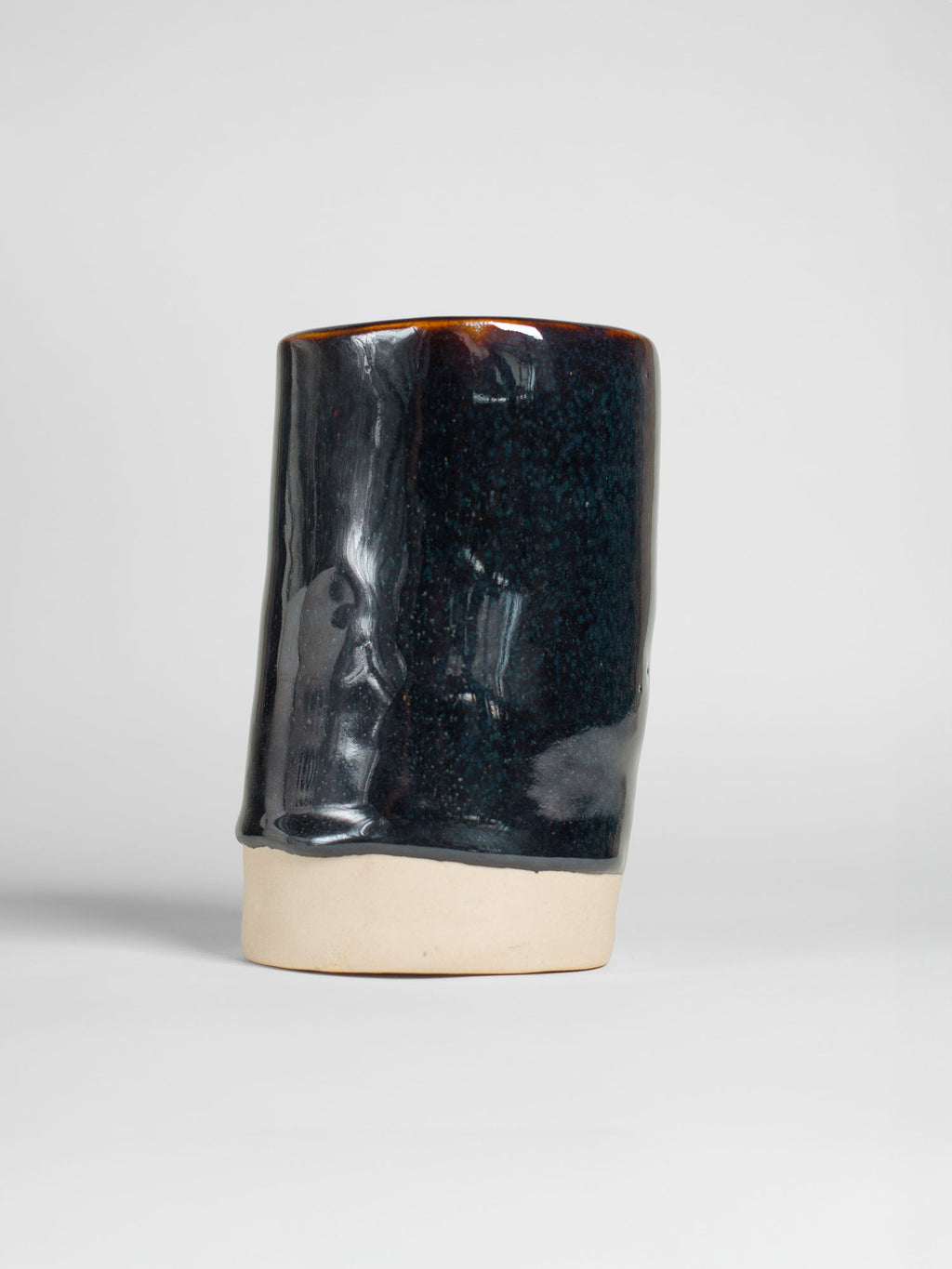 Tea Dust on a thrown cylinder, glossy blue-black breaking to amber at the rim over a raw clay foot