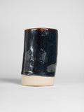 Tea Dust on a thrown cylinder, glossy blue-black breaking to amber at the rim over a raw clay foot