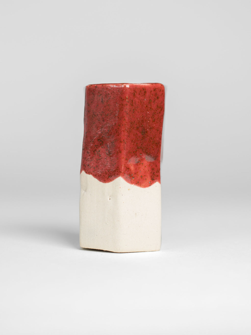 Cranberry Red test tile on white clay, speckled red with a scalloped glaze line above bare clay