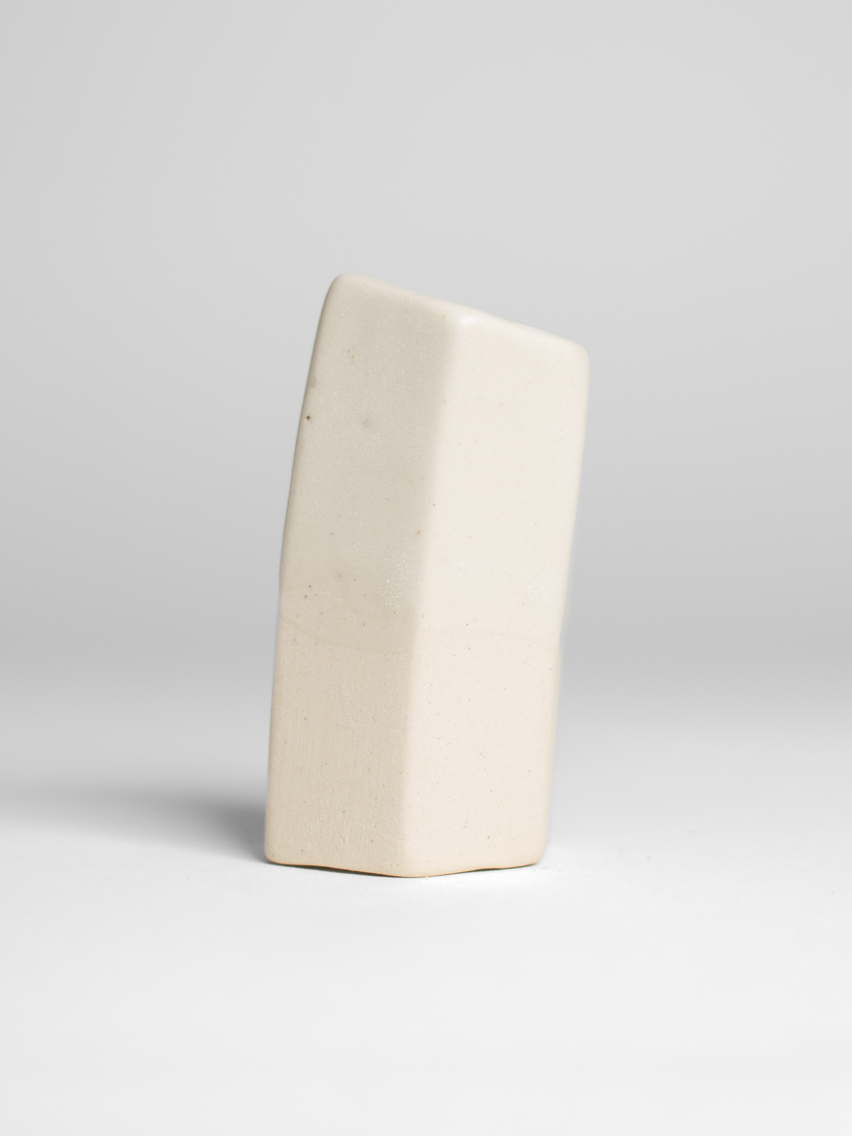 A handmade ceramic object with a tall, cylindrical shape. The upper portion is glazed with milky matt white. The cylinder features an artistic, organic design with a matte finish.