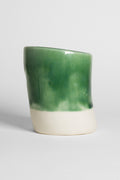 A handmade ceramic object with a slightly tilted cylindrical shape. The upper half is glazed in a glossy, vibrant green with subtle variations in tone, while the bottom part is unglazed, revealing the natural off-white colour of the clay. The design is simple yet artistic with a smooth, polished finish.
