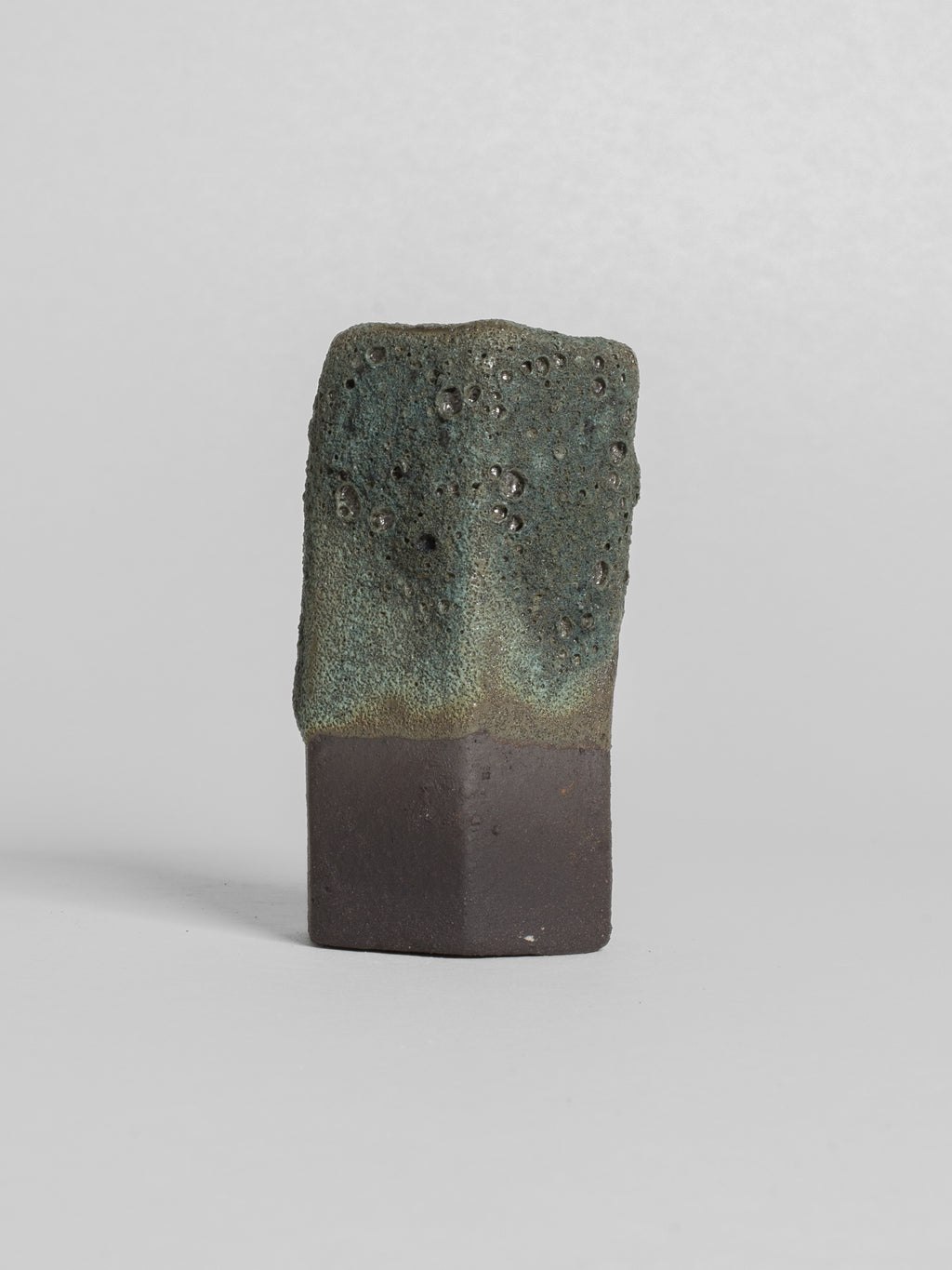 Lichen Grey test tile on dark clay, heavy crater texture fading to a smooth band above the foot