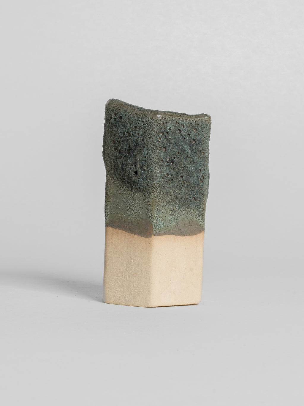 Lichen Grey test tile on pale clay, cratered green-grey with a soft edge where the glaze stops