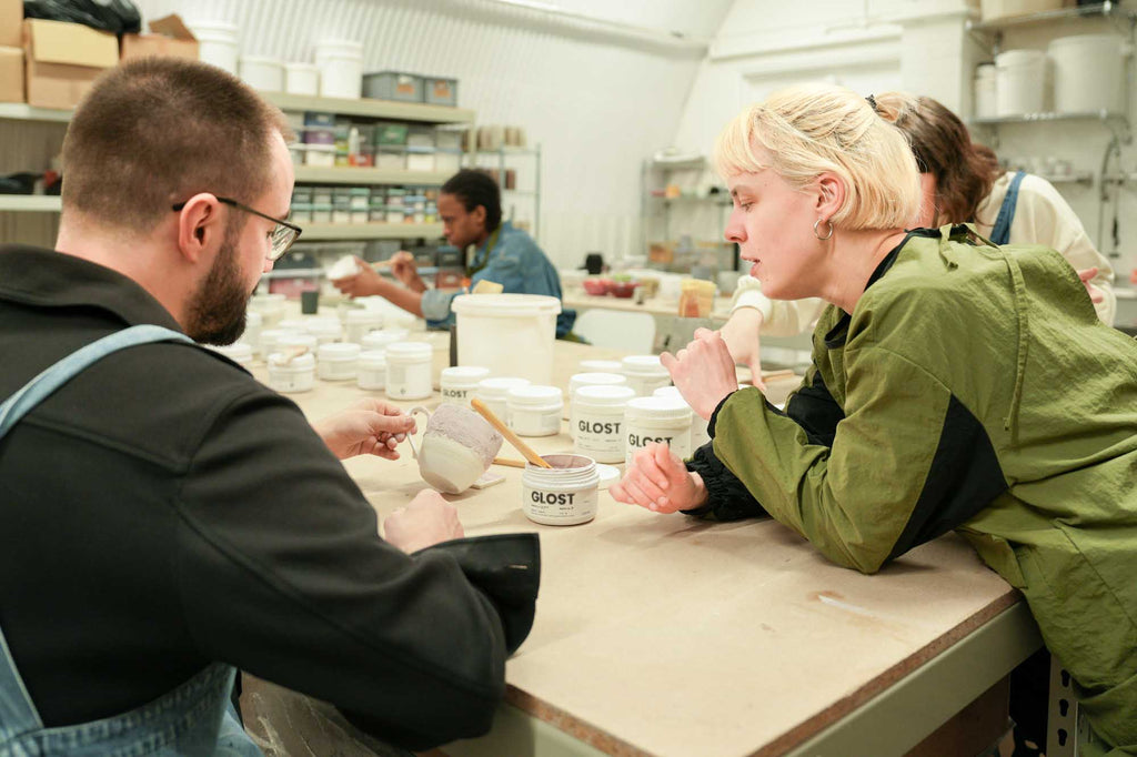 Two people working at a table with pottery glazes in a studio workshop setting