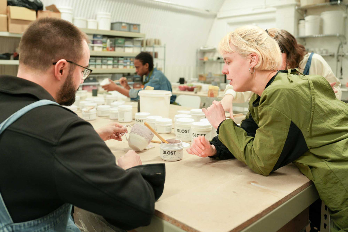 Two people working at a table with pottery glazes in a studio workshop setting