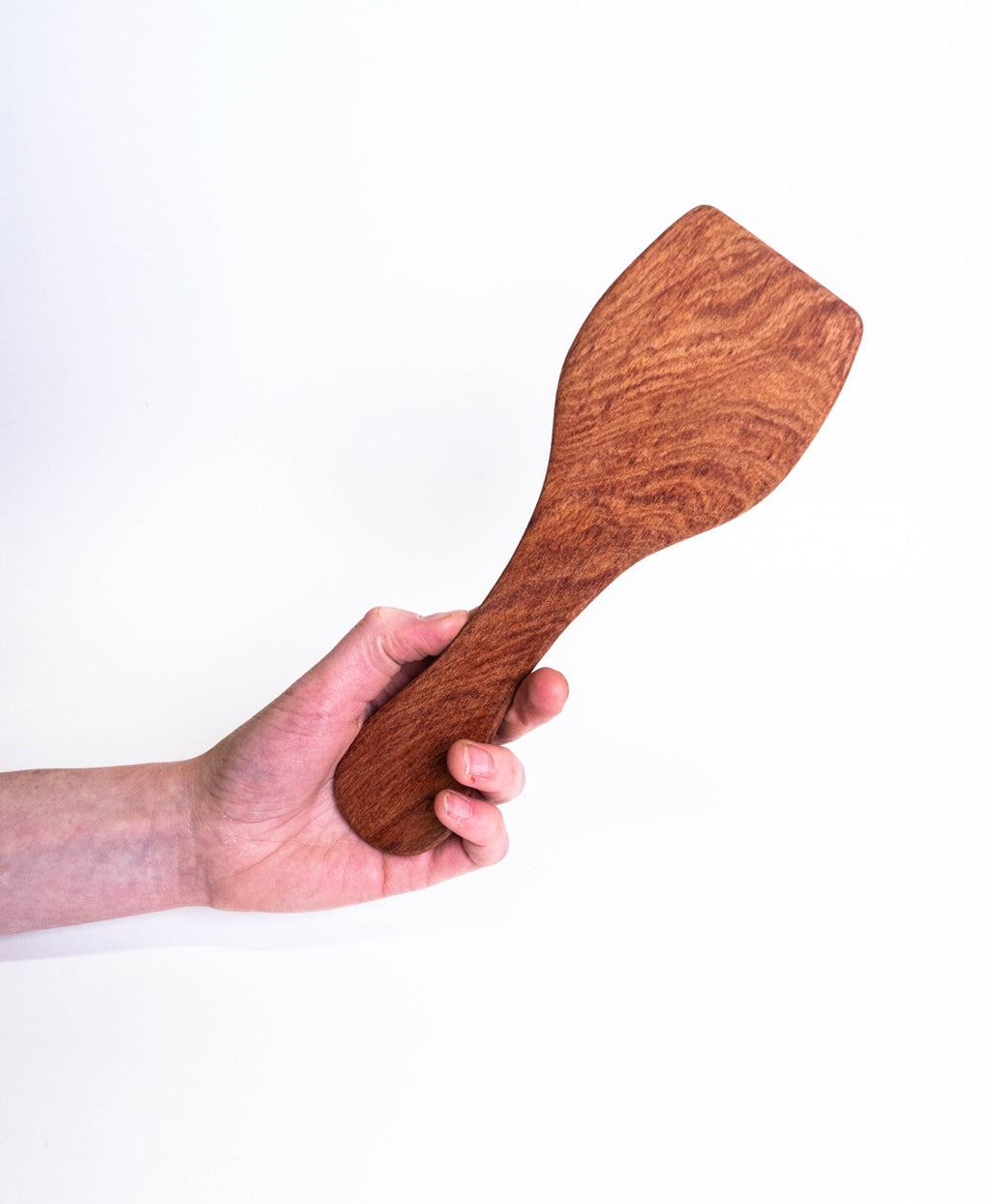Hand holding a figured hardwood paddle, showing its size against the forearm