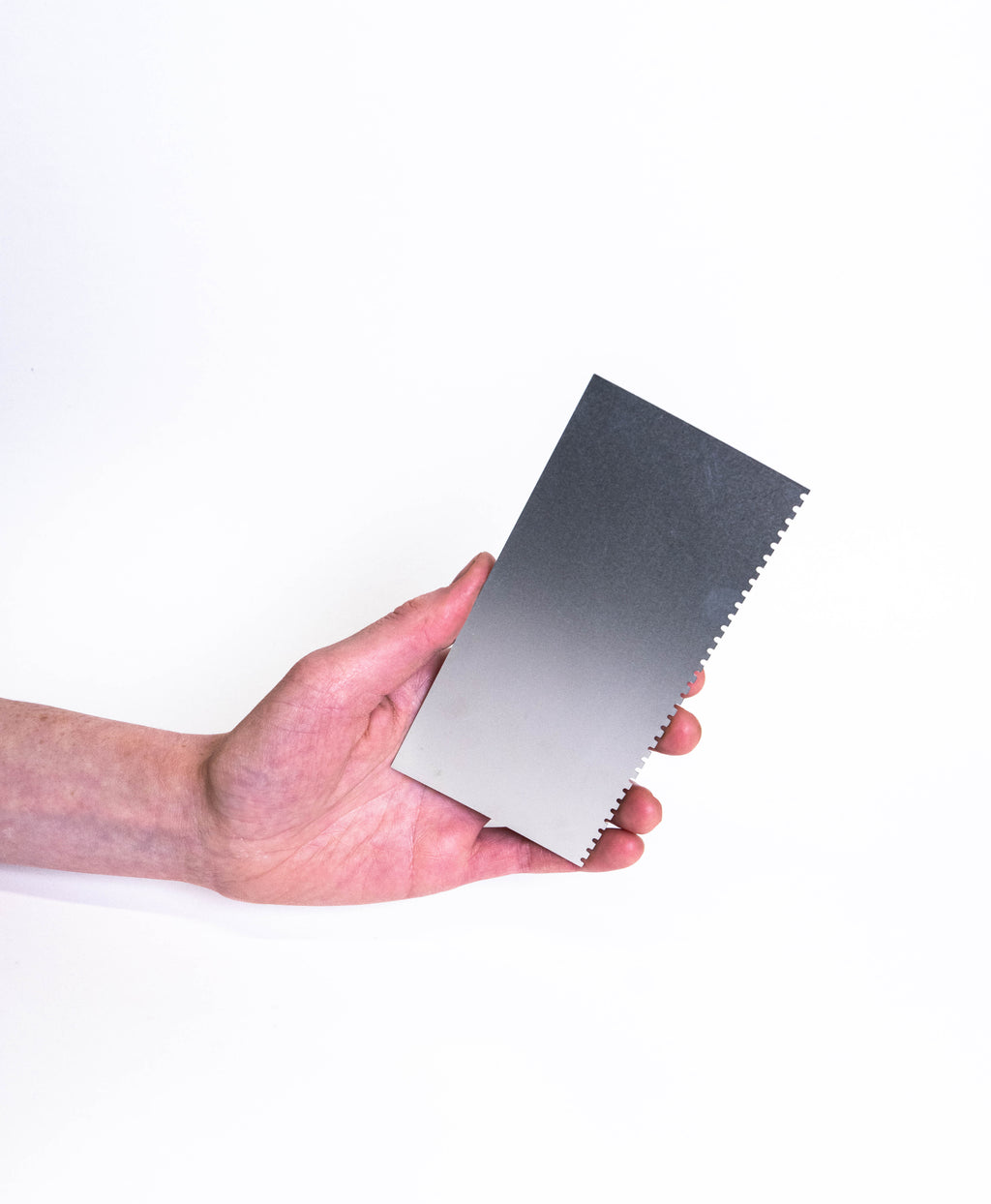 Hand holding the large rectangular steel rib, toothed along one long edge