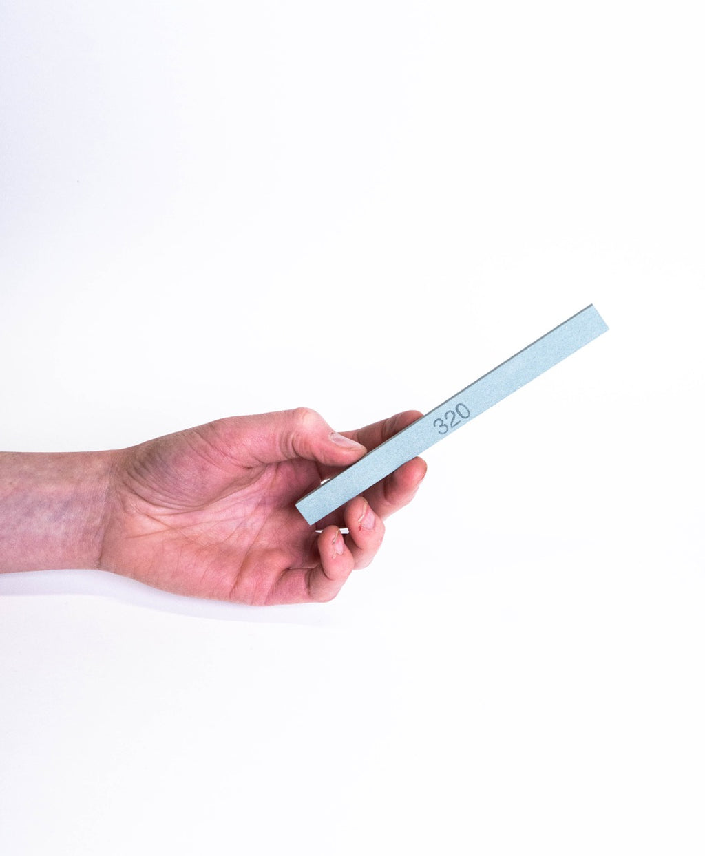 A hand holding a 320 grit whetstone stick in pale blue-grey, for sharpening pottery tools.
