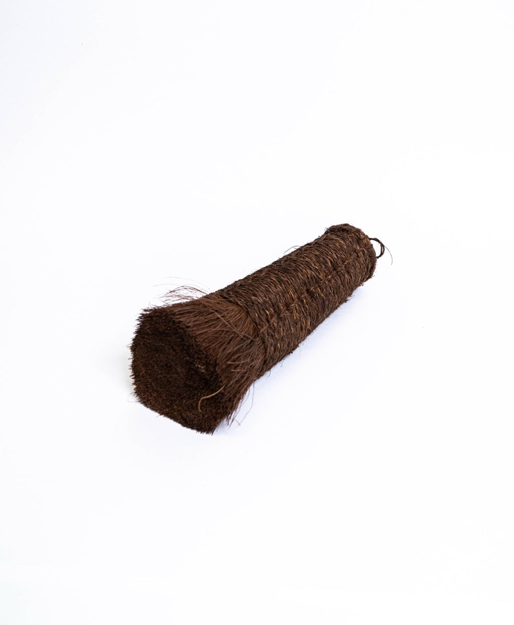 Long tapered palm fibre brush with stitched binding, lying on its side