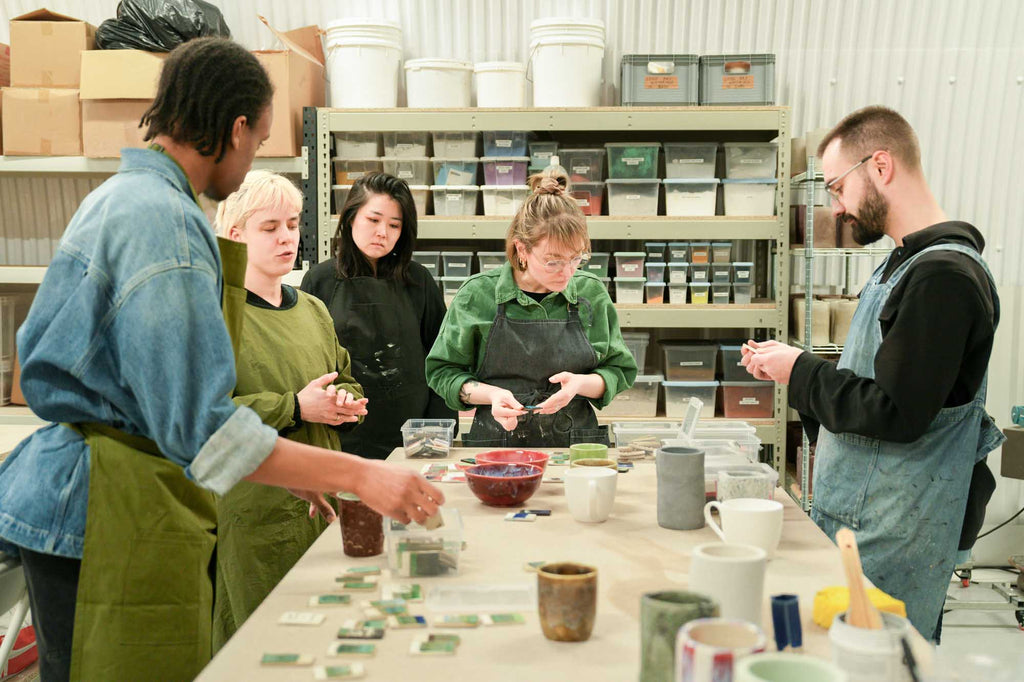 Group of people in a pottery workshop with ceramci glaze samples on a table.
