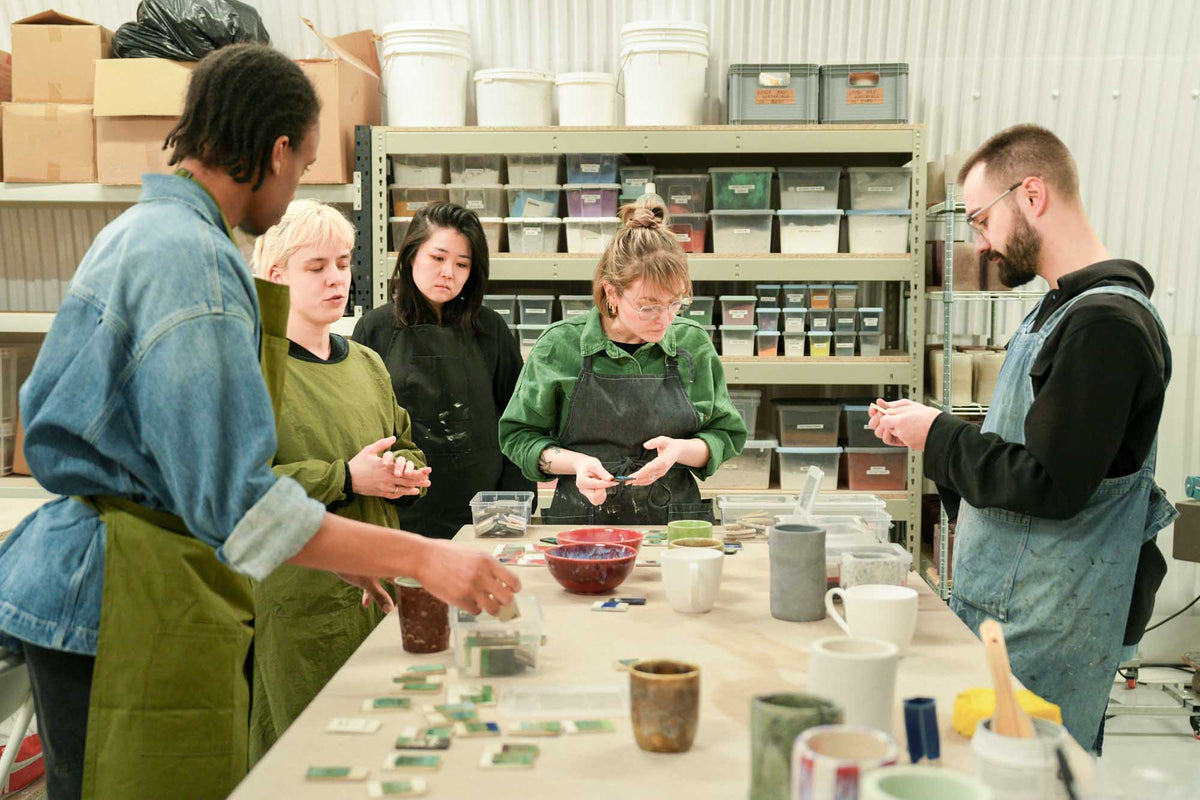 Group of people in a pottery workshop with ceramci glaze samples on a table.