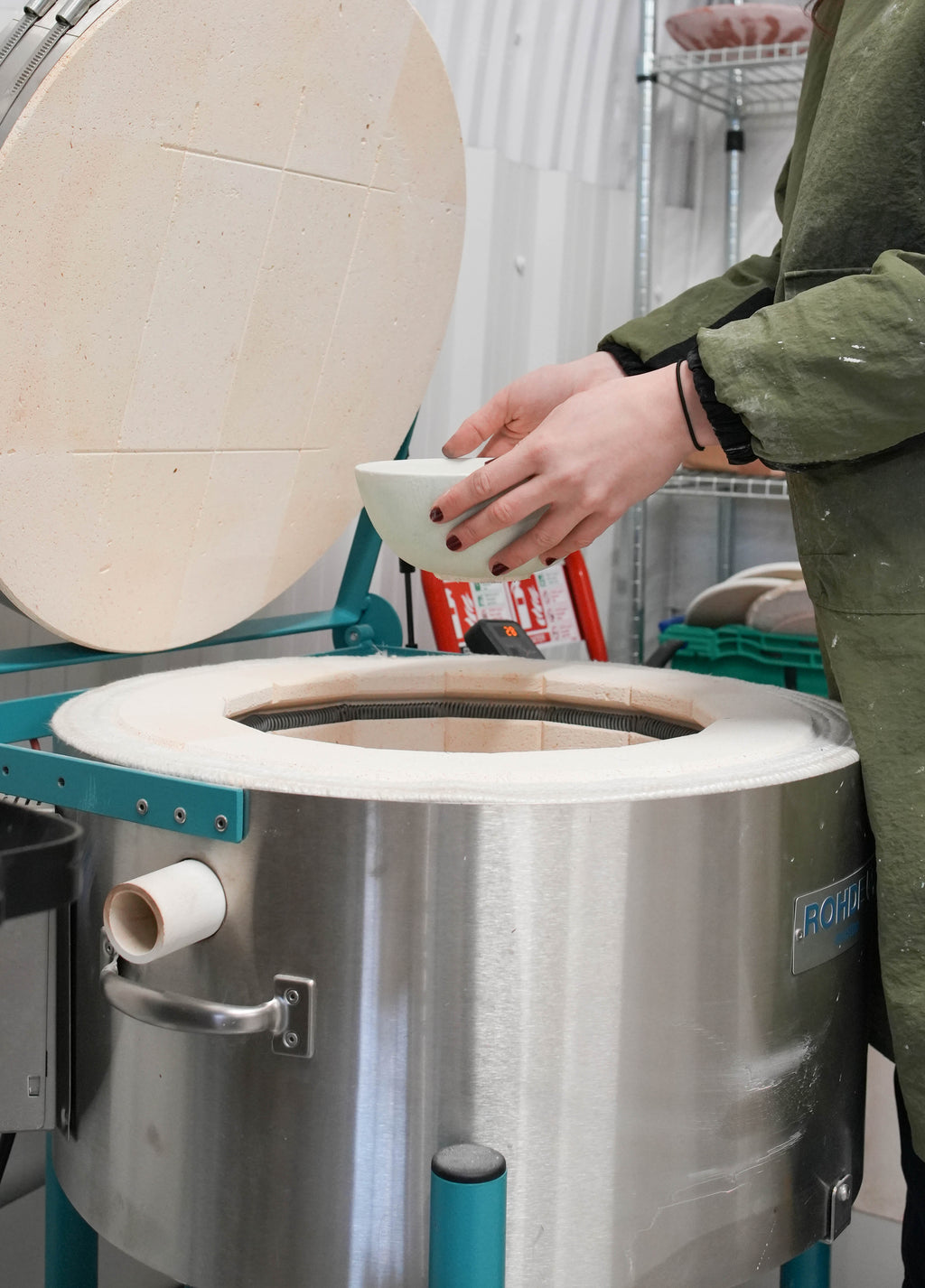 A gloved hand lowering a ceramic bowl into an electric kiln.