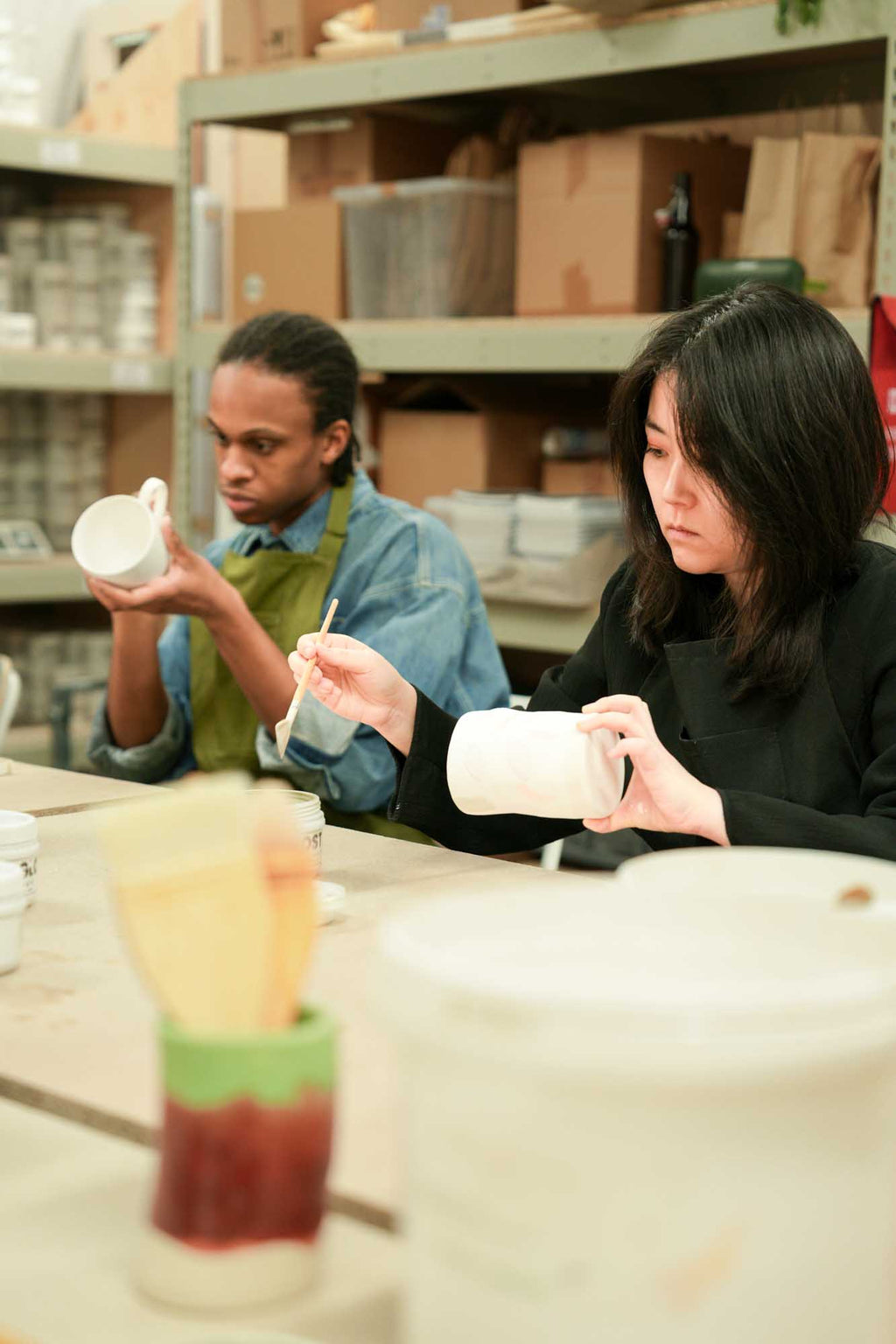 Two people brushing a pottery glaze during a workshop