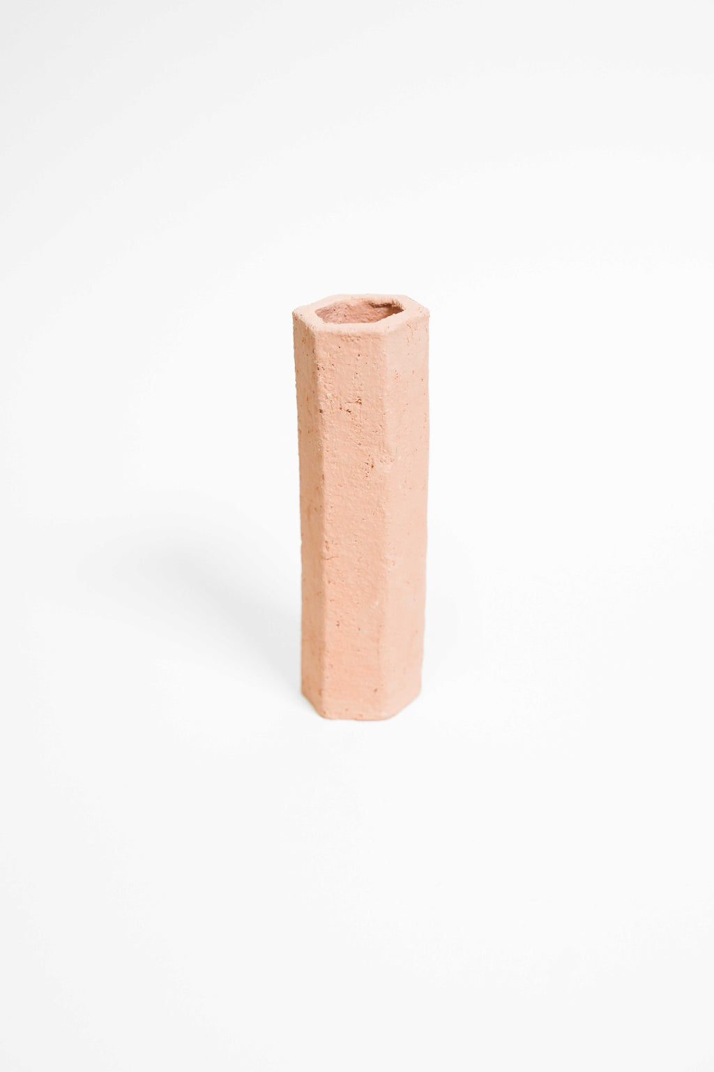 A tall faceted vessel hand-built in Crank, unglazed pink terracotta with a rough grogged surface