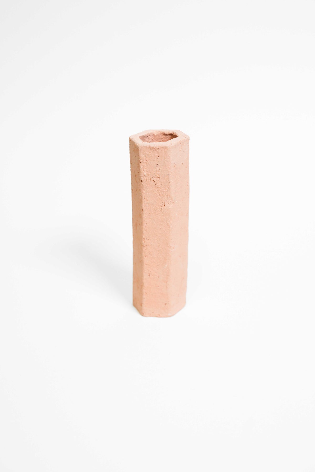 A tall faceted vessel hand-built in Crank, unglazed pink terracotta with a rough grogged surface