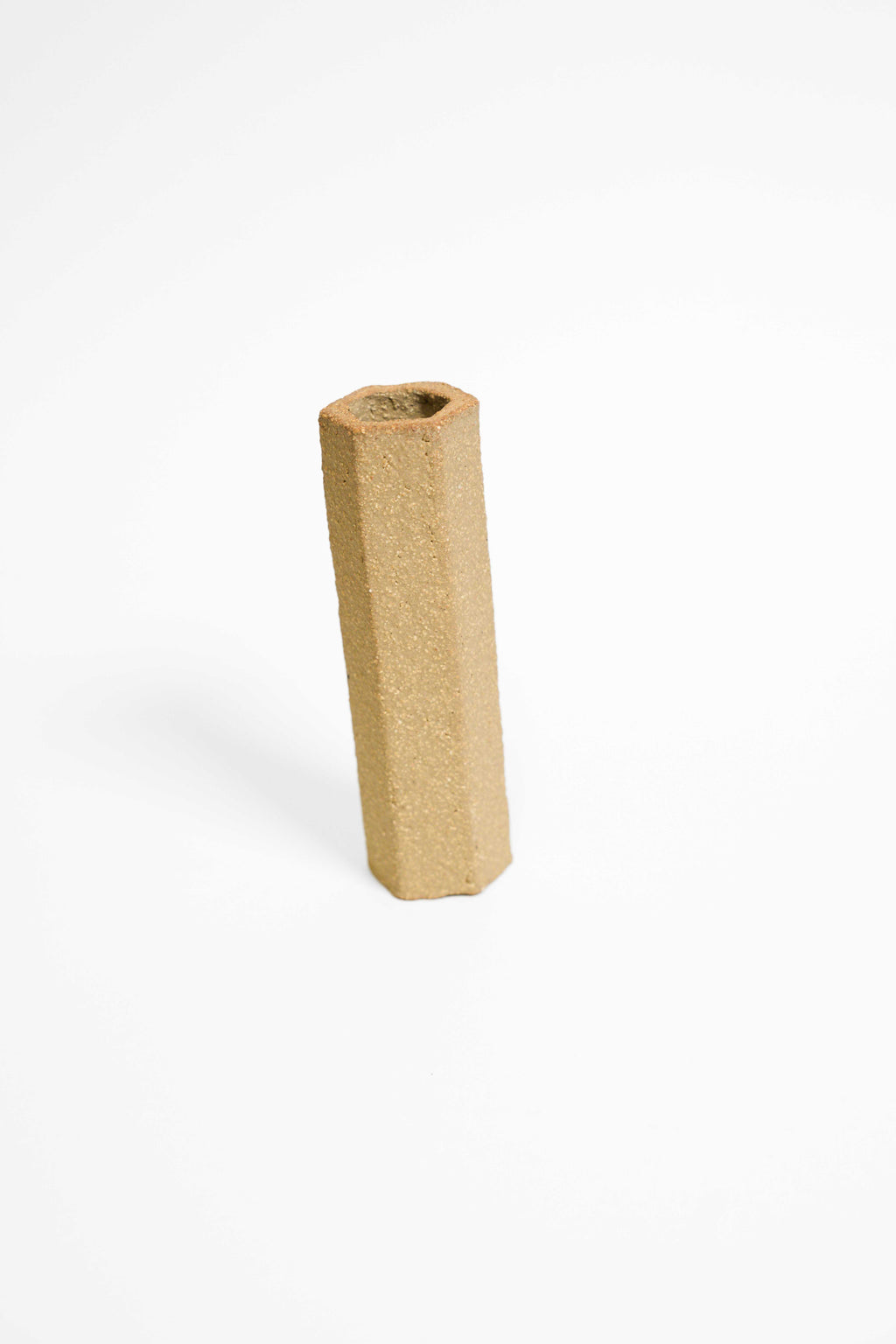 A tall faceted vessel in Crank fired higher, olive buff with an open sandy texture
