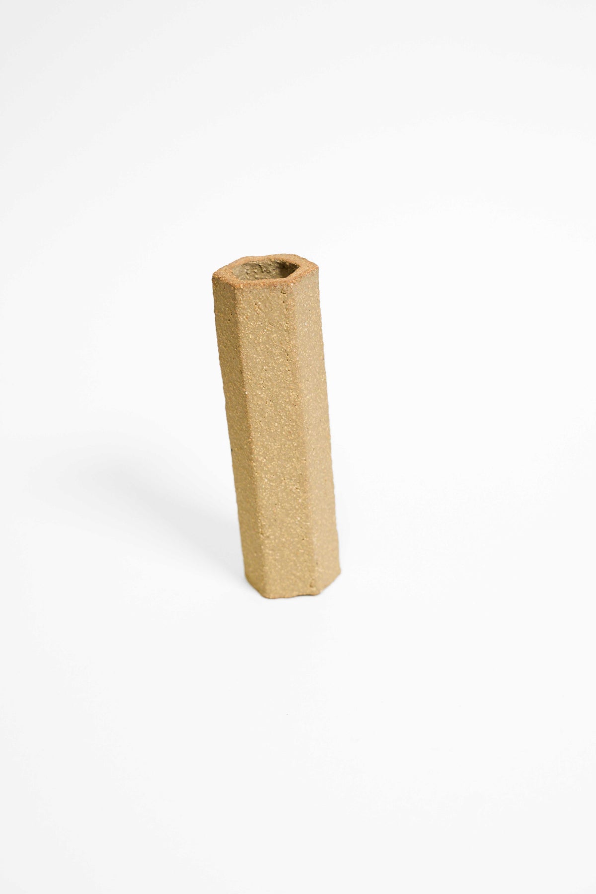 A tall faceted vessel in Crank fired higher, olive buff with an open sandy texture