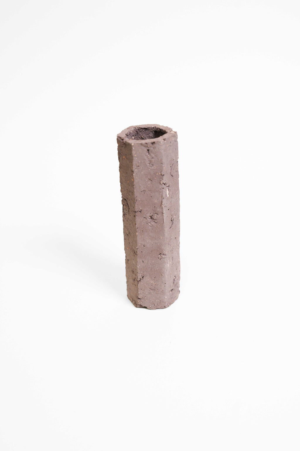 A tall faceted vessel hand-built in PF660, unglazed plum-brown with a rough pitted surface