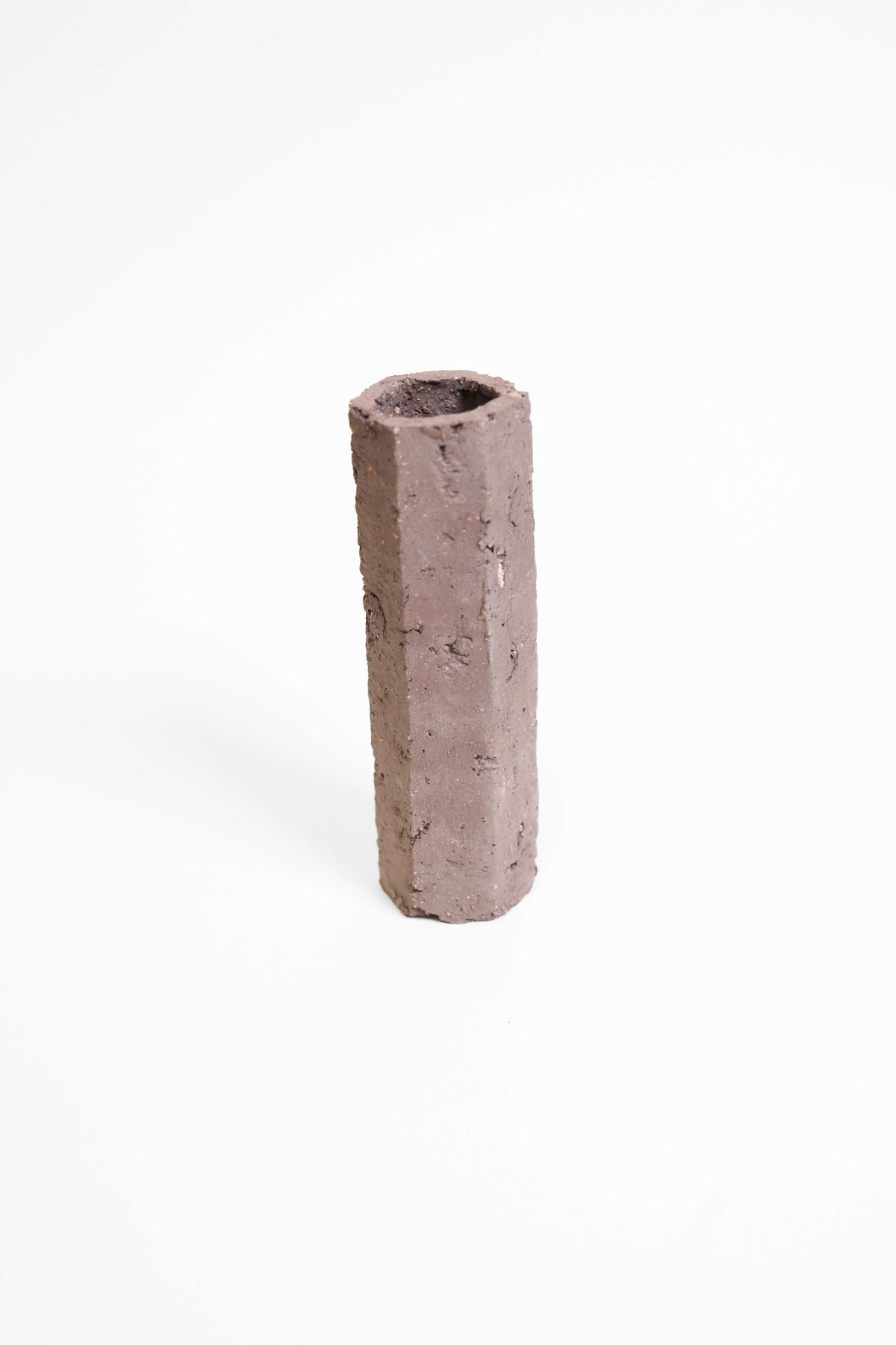 A tall faceted vessel hand-built in PF660, unglazed plum-brown with a rough pitted surface