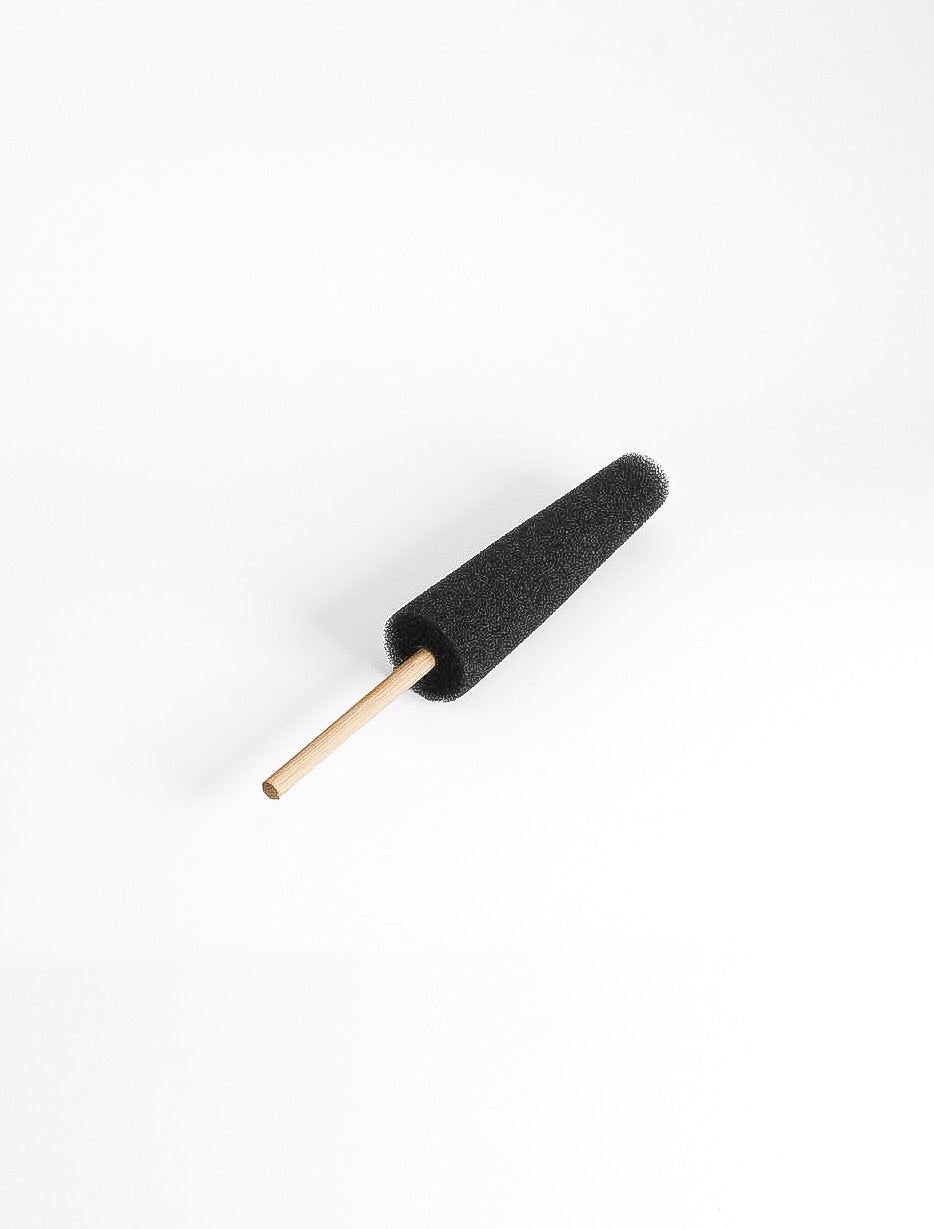 The black sponge on a stick laid flat, showing the tapered foam head and the thin wooden handle.