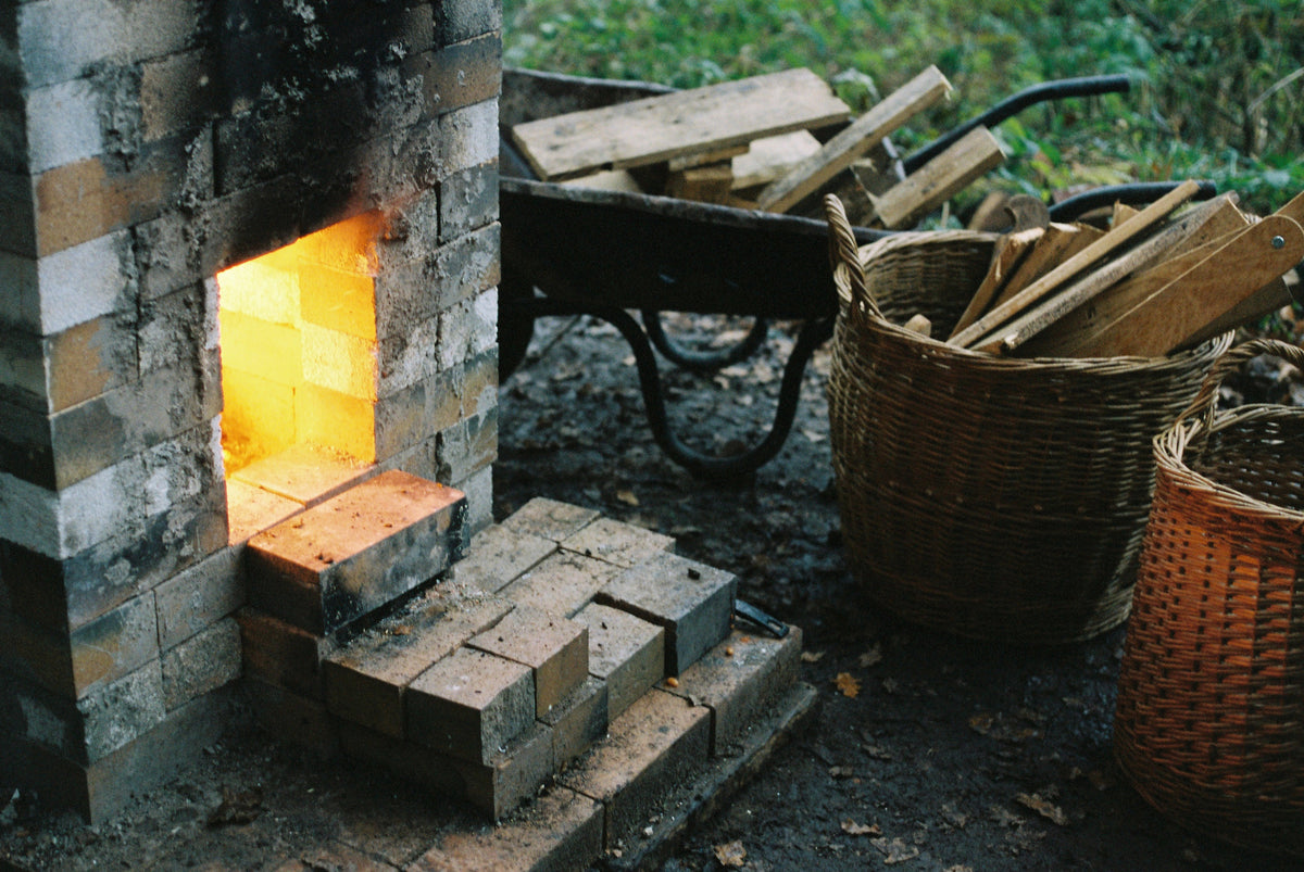 The stoking hole of a wood fired kiln, with firewood beside it in a wheelbarrow and baskets